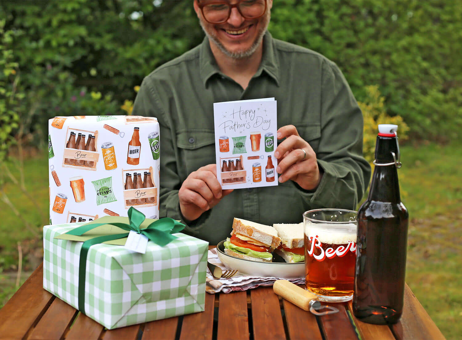 Man celebrating with Fathers Day gifts for 2025, holding a card and surrounded by wrapped presents, food, and drinks.