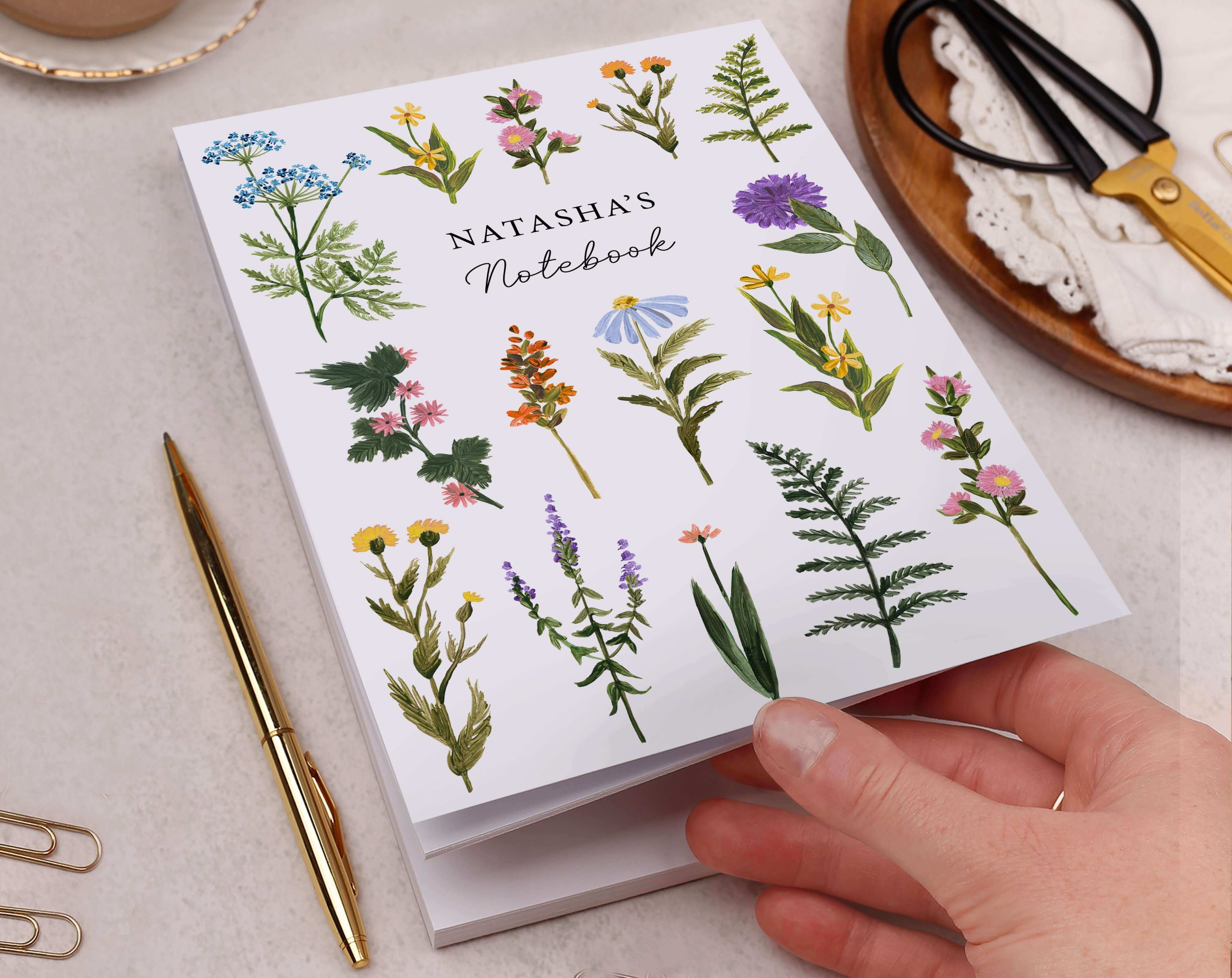 A hand holding a floral notebook titled 'Natasha's Notebook' illustrating the difference between stationery vs stationary.