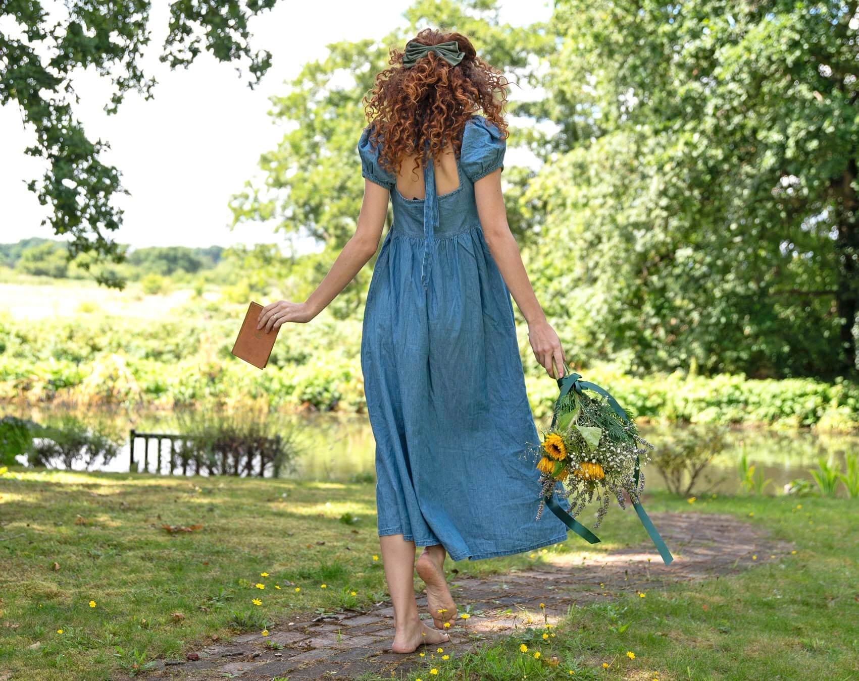 Woman in a blue dress walking by a lake with flowers, symbolizing Flower Meanings and their significance.