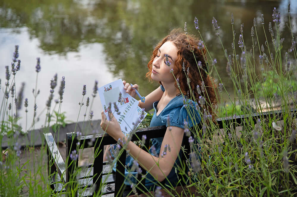 Young woman creating Nature Inspired Designs while sitting in a meadow surrounded by lavender flowers.