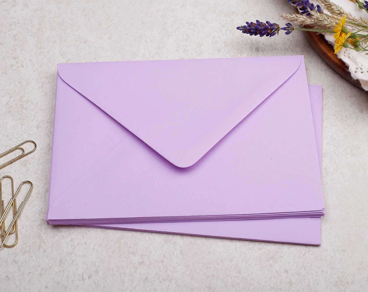 Coloured Envelopes in lilac color stacked on a table with paper clips and lavender.