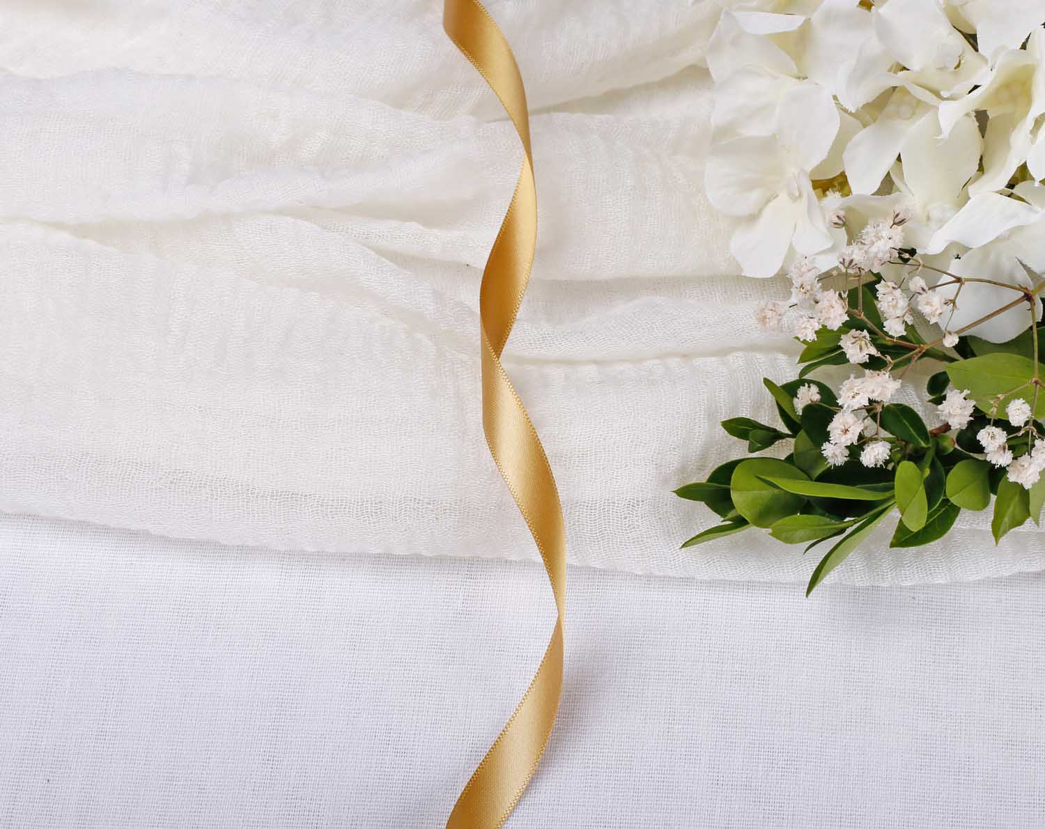 Antique Gold Satin Ribbon For Wedding elegantly placed on textured fabric with flowers in the background.