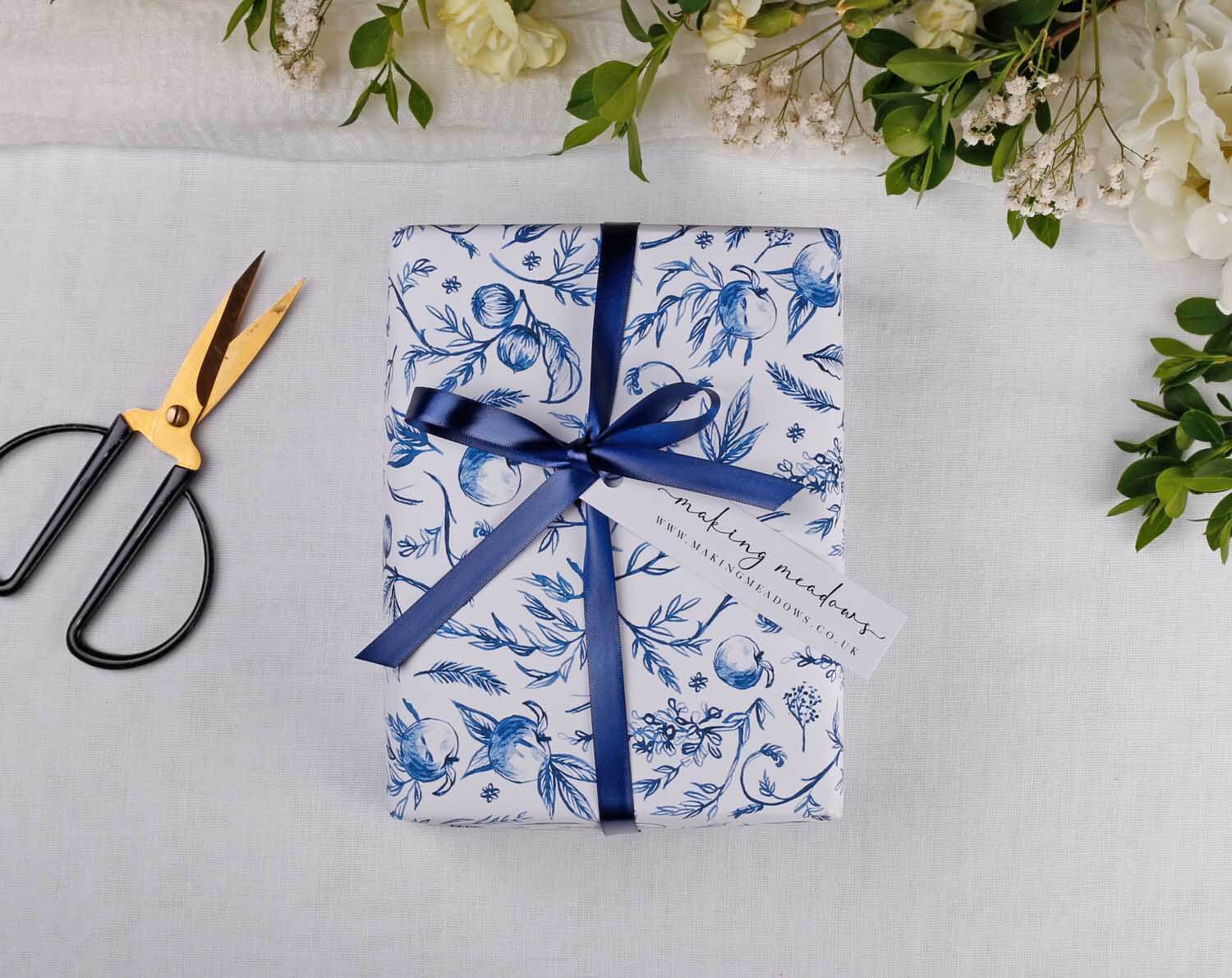 Blue Garden Wedding Wrapping Paper with navy ribbon and scissors on a table surrounded by flowers.