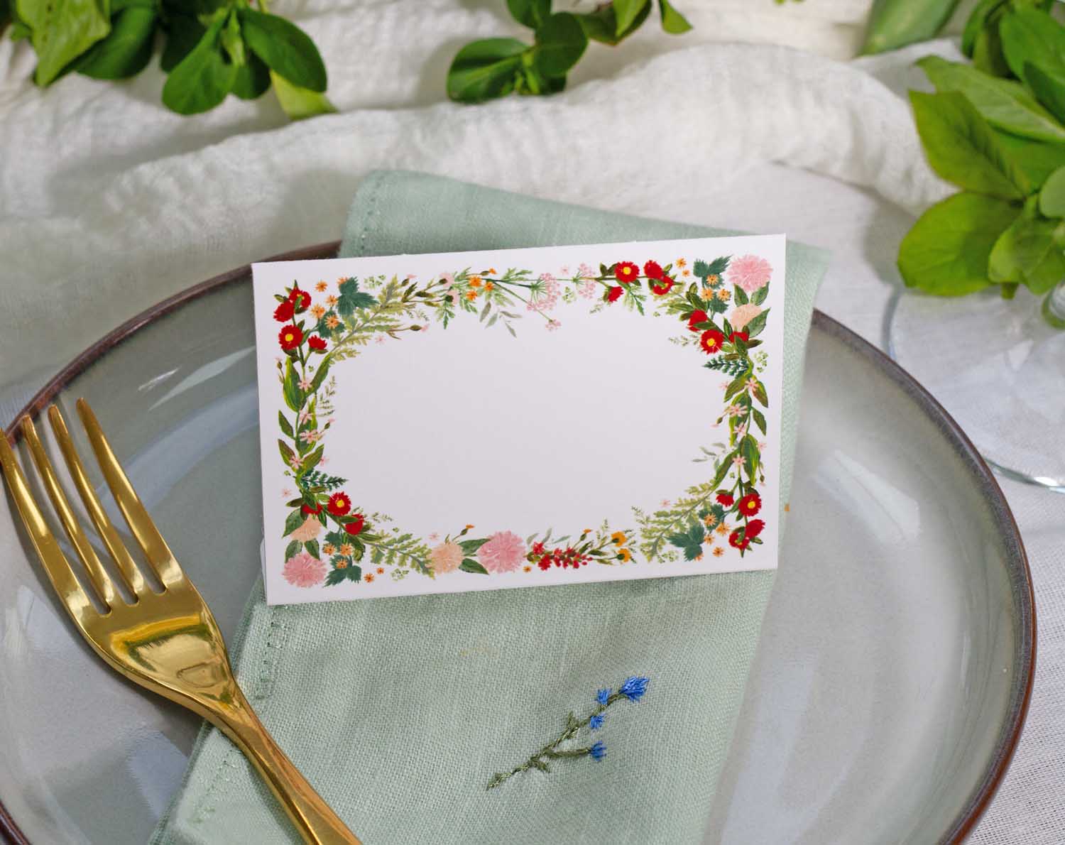 Boho Wedding Place Cards with floral design on a table setting featuring a green napkin and gold fork.