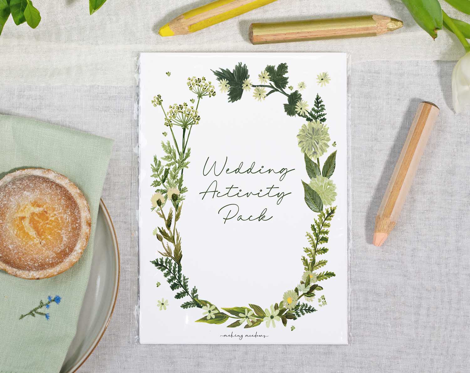 Botanical Wedding Kids Activity Pack on a table with greenery and coloring pencils, perfect for entertaining kids at weddings.