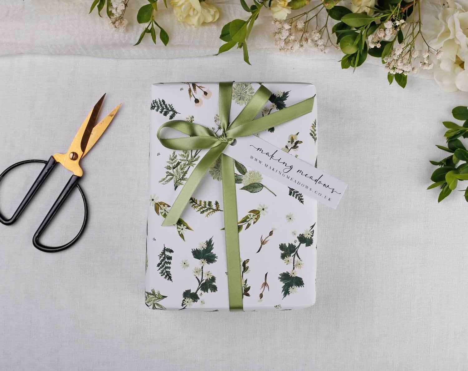 Botanical Wedding Wrapping Paper beautifully wrapped with green ribbon and tag, surrounded by floral decor and scissors.