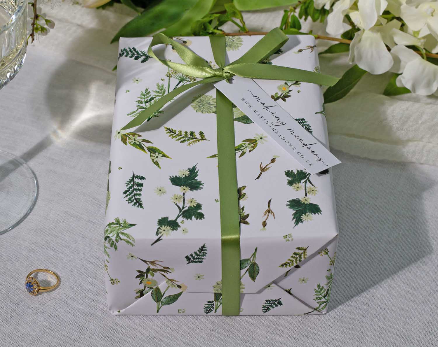 Botanical Wedding Wrapping Paper elegantly wrapped gift with green ribbon and tag on a table with decor.
