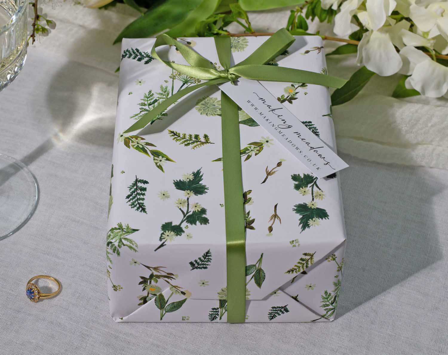 Botanical Wedding Wrapping Paper elegantly wrapped gift with green ribbon and tag on a table with decor.