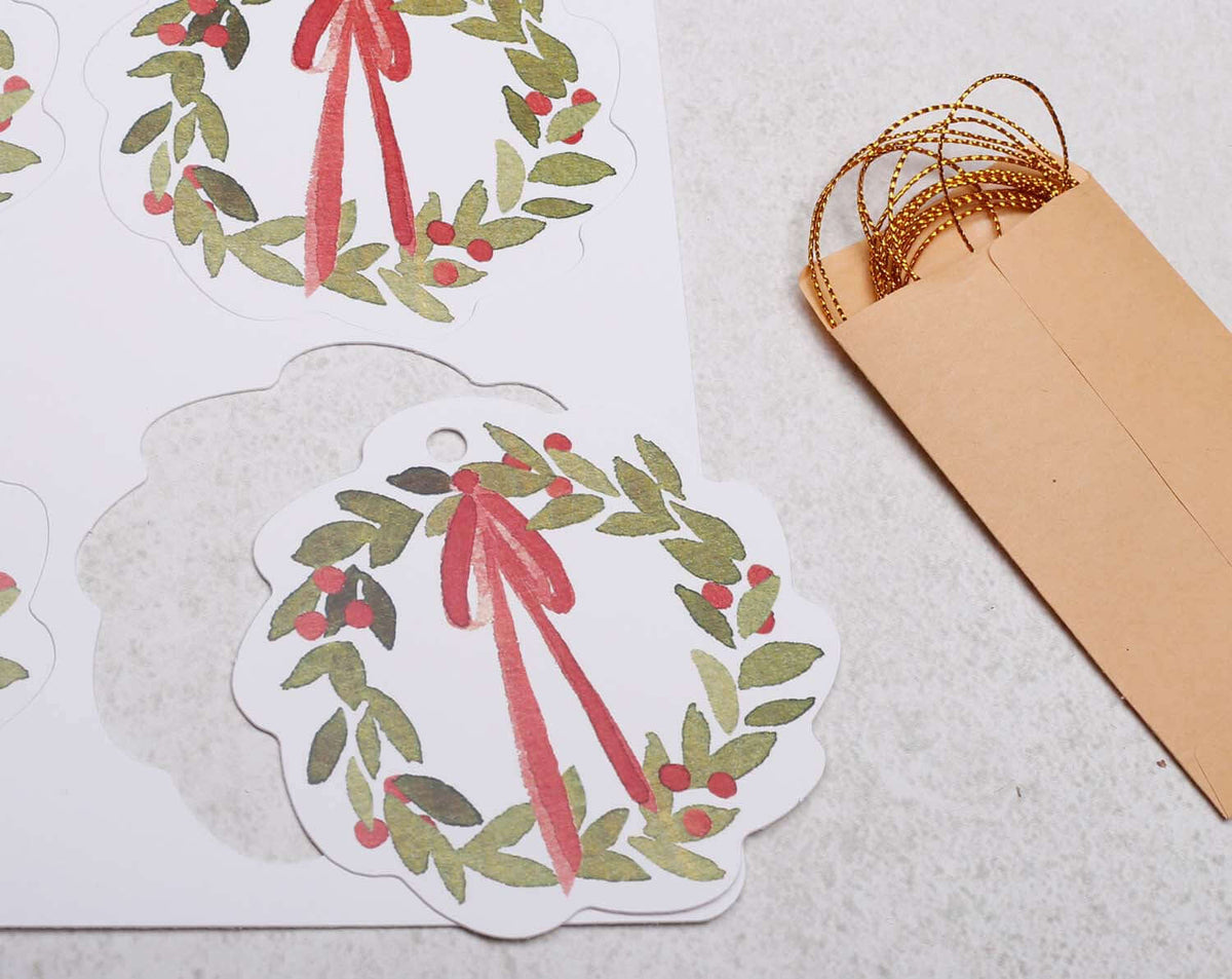 Wreath Christmas Gift Tags featuring floral designs with red ribbons and brown kraft envelopes.