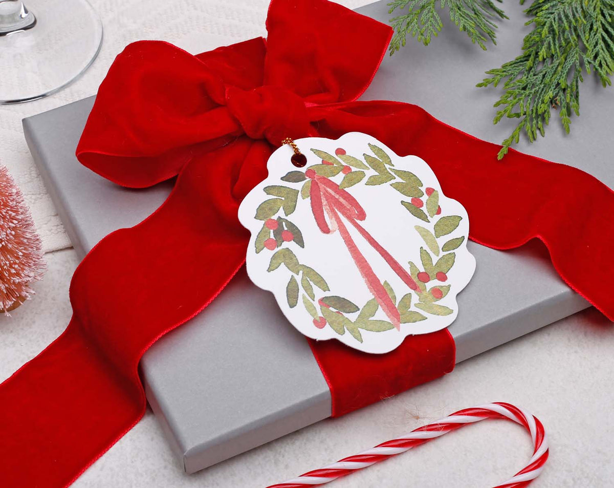Wreath Christmas Gift Tags attached to a beautifully wrapped gift with a red ribbon and festive decorations.
