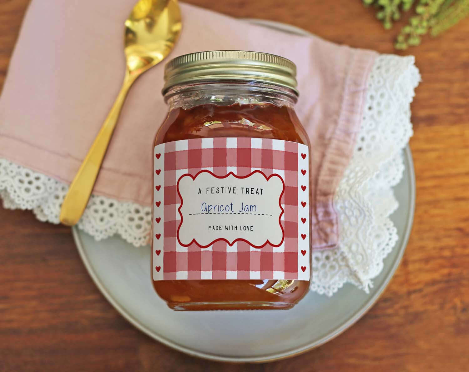 Christmas Jam Jar Labels With Red Gingham on an apricot jam jar, styled with a gold spoon and pink napkin.