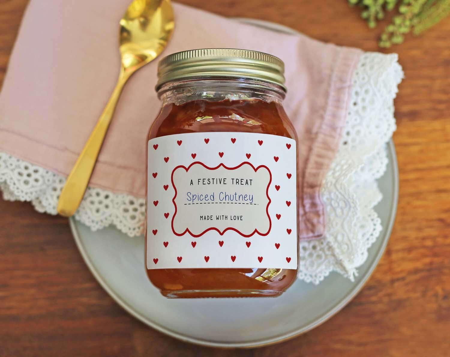 Christmas Jam Jar Labels With Red Hearts on a jar of spiced chutney, styled with a golden spoon and a napkin.