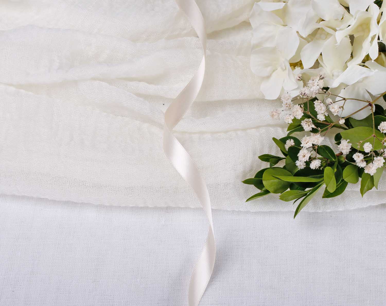 Cream Ivory Satin Ribbon For Wedding on a textured fabric with flowers and greenery, perfect for elegant decorations.