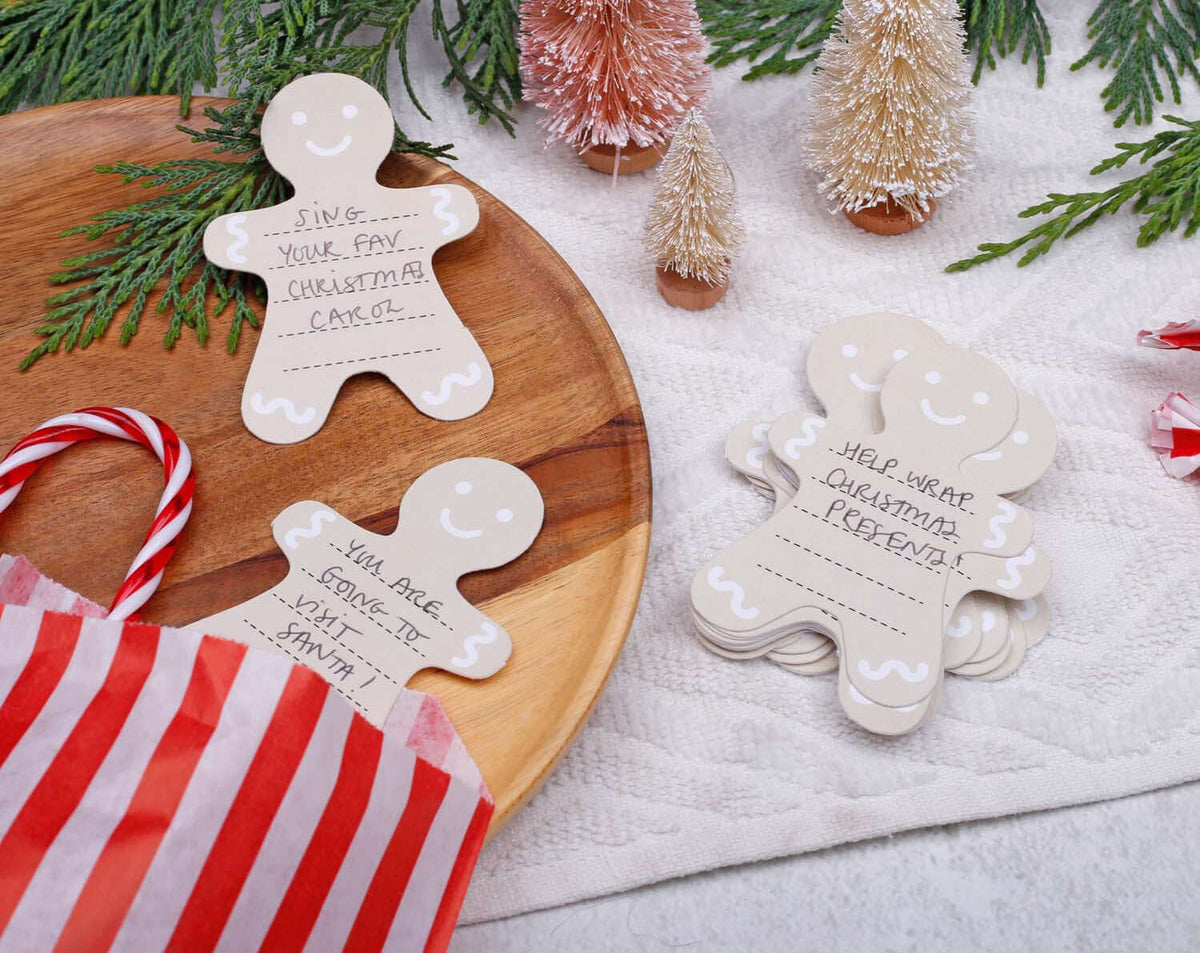 Gingerbread Fill Your Own Activity Cards on a wooden platter surrounded by festive decor and a gift bag.