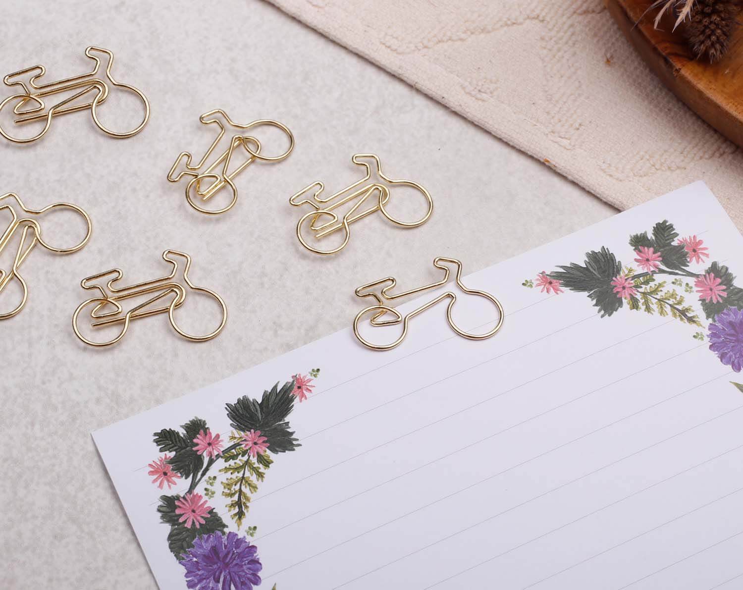 Gold Bicycle Paper Clips arranged on a decorative notepad with floral design.