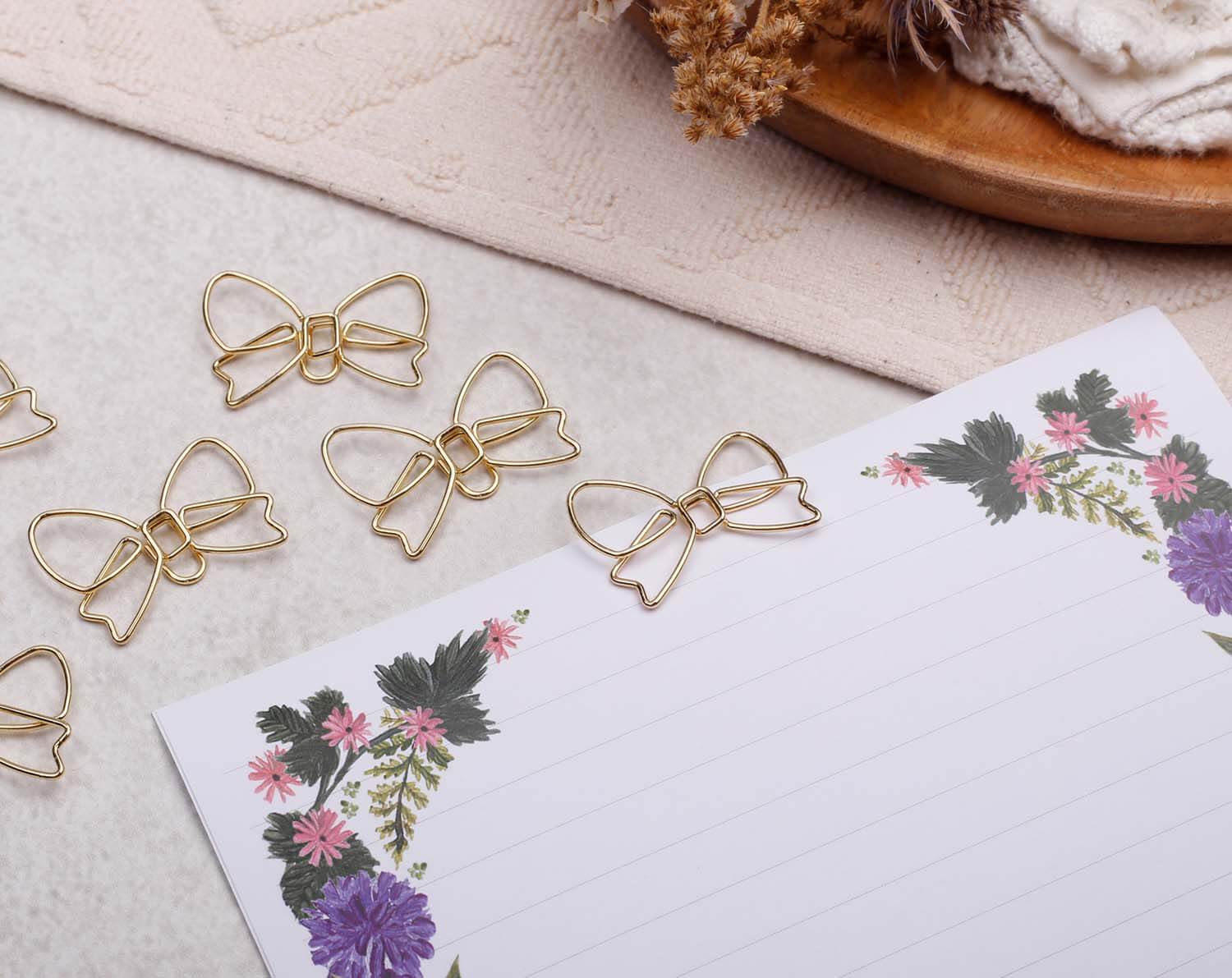 Gold Bow Paper Clips arranged on floral stationery, showcasing their unique bow shape and shiny gold finish.