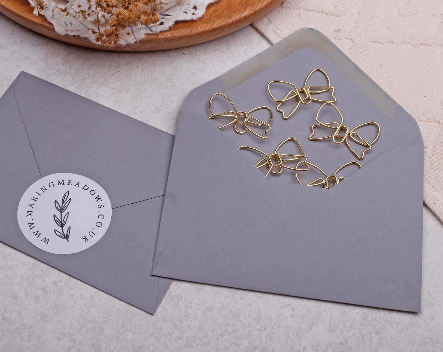 Gold Bow Paper Clips displayed inside a gray envelope, showcasing their unique bow shape and shiny finish.