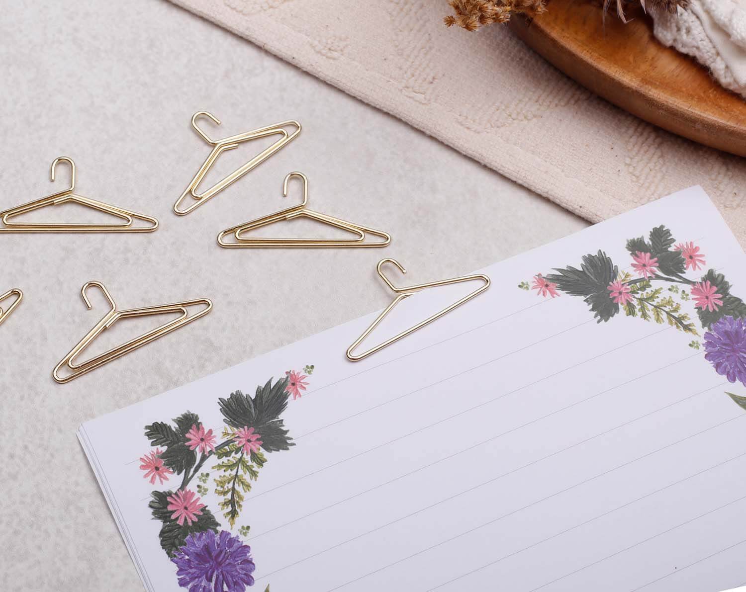 Gold Coat Hanger Paper Clips on a floral-themed notepad for fun and quirky stationery.