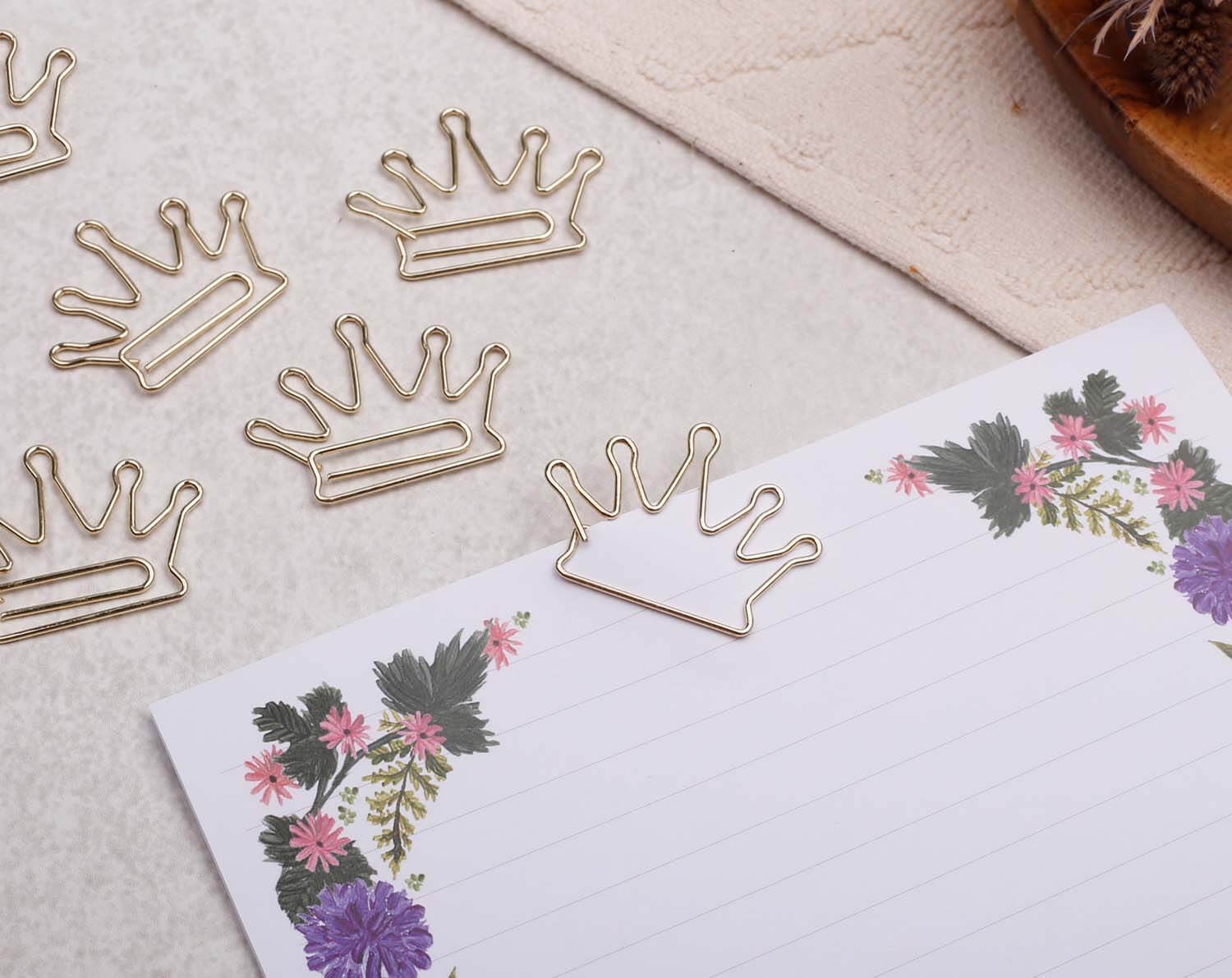 Gold Crown Paper Clips shaped like crowns atop floral notepad, adding elegance to stationery.