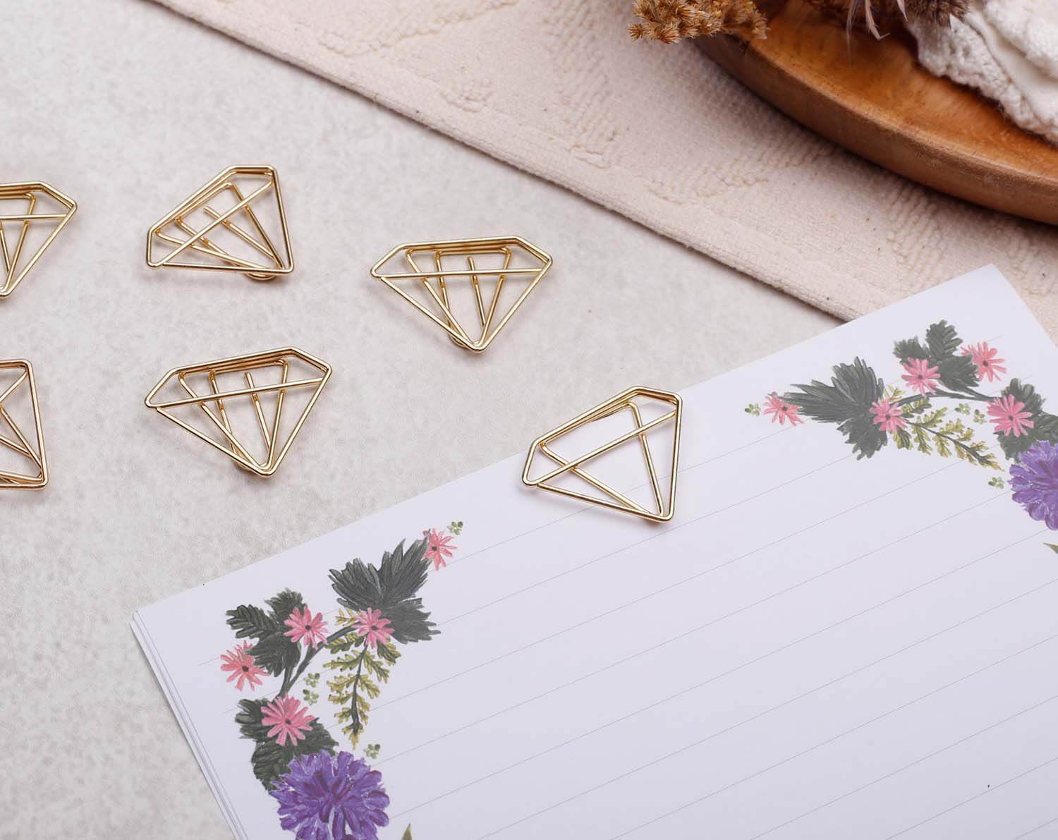 Gold Diamond Paper Clips shaped like diamonds placed on floral stationery paper.