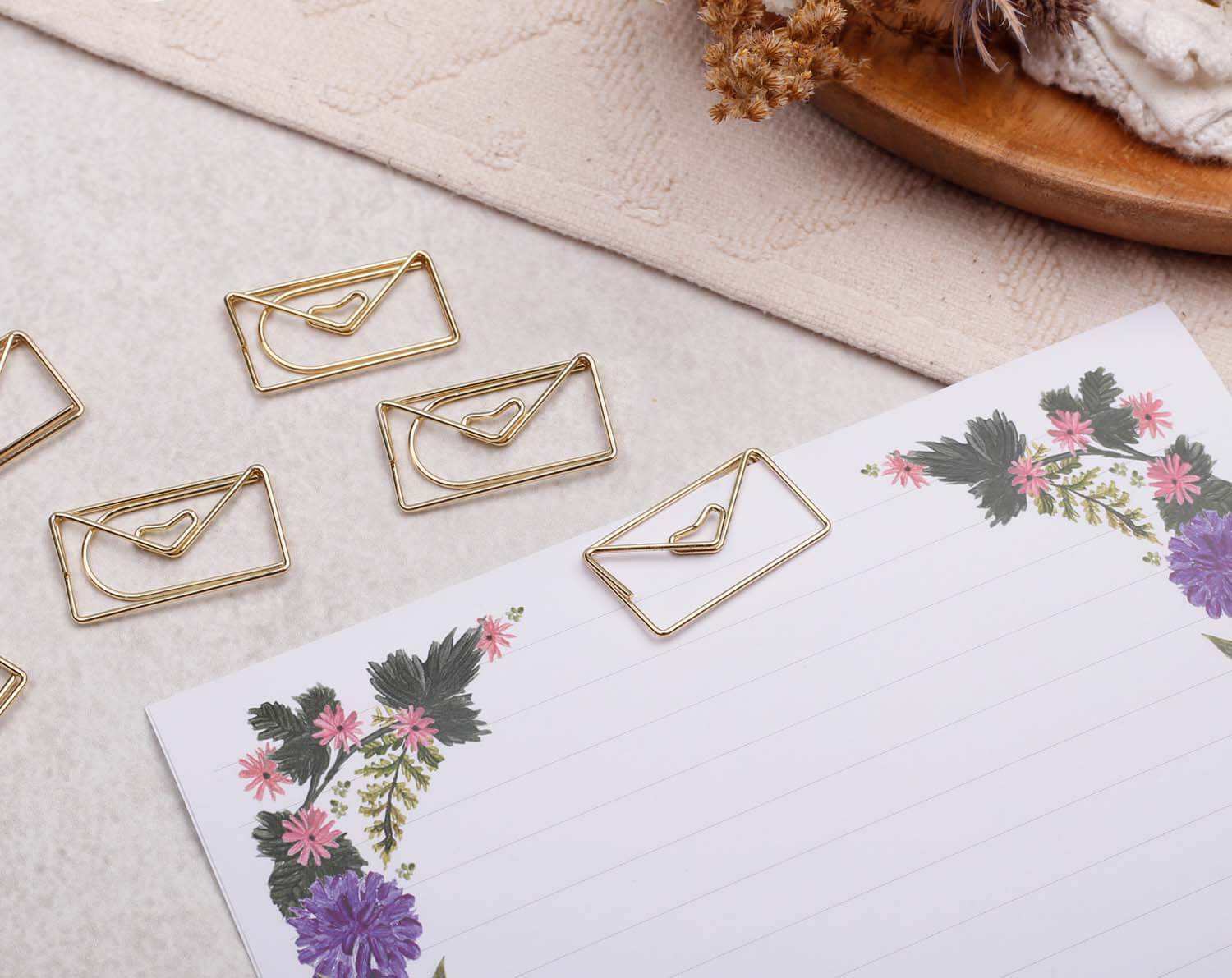 Gold Envelope Paper Clips laid next to decorative stationery with floral design.