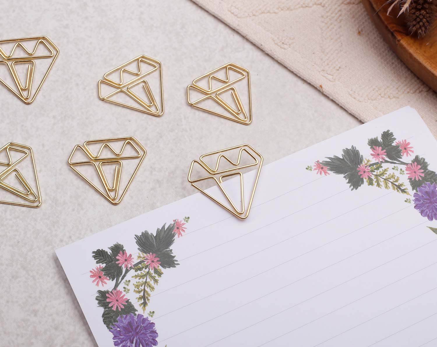 Gold Gem Paper Clips in unique gem-shaped designs on a floral notepad.