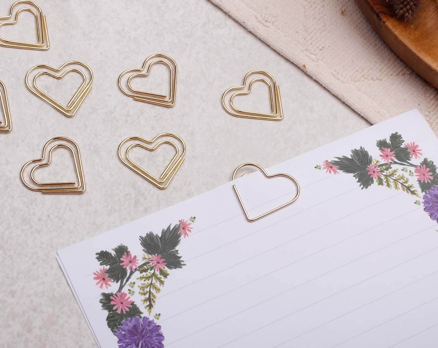 Gold Heart Paper Clips beautifully arranged next to a floral notepad on a textured surface.