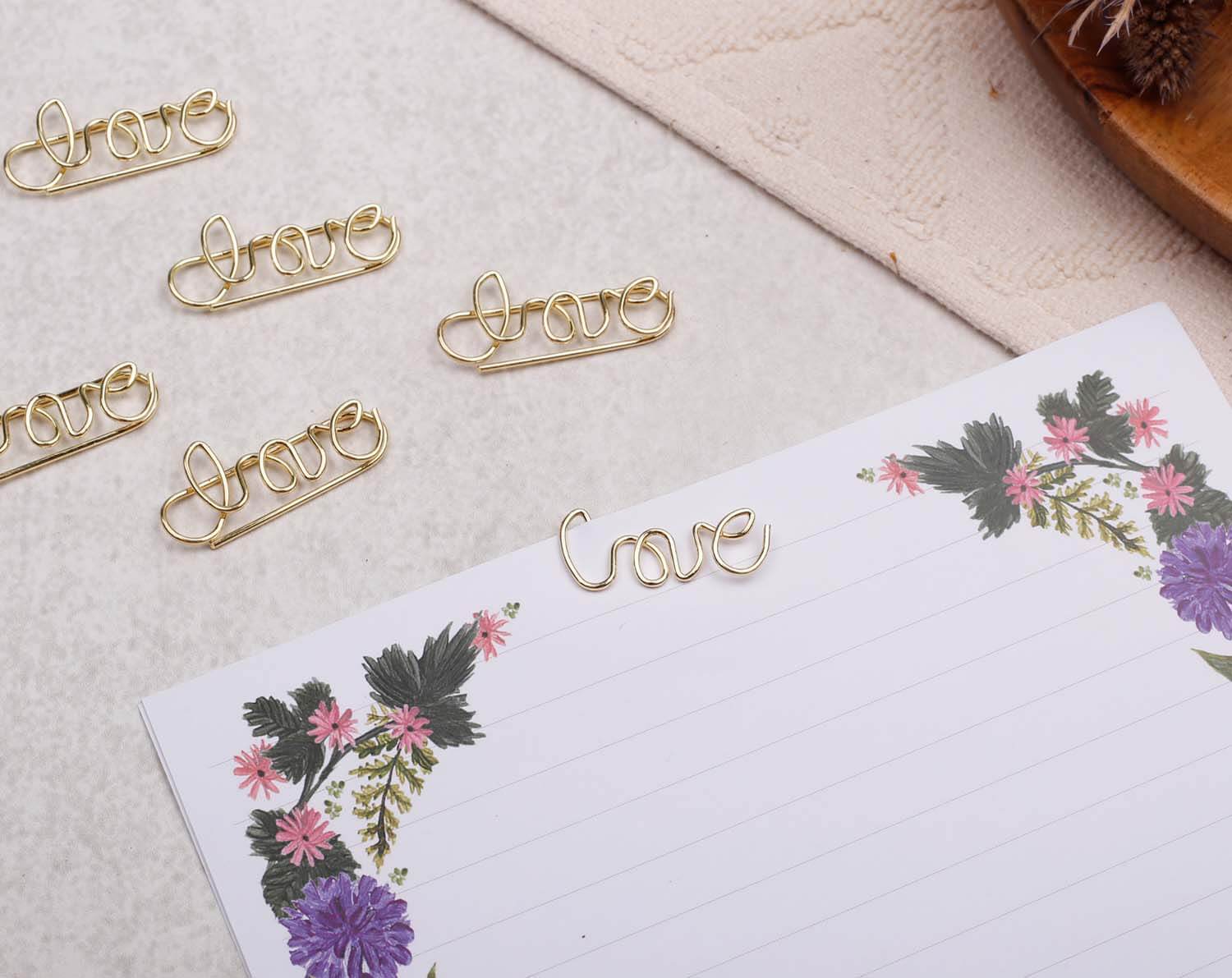Gold Love Paper Clips - Shaped arranged on a floral notepad, enhancing stationery with a romantic touch.