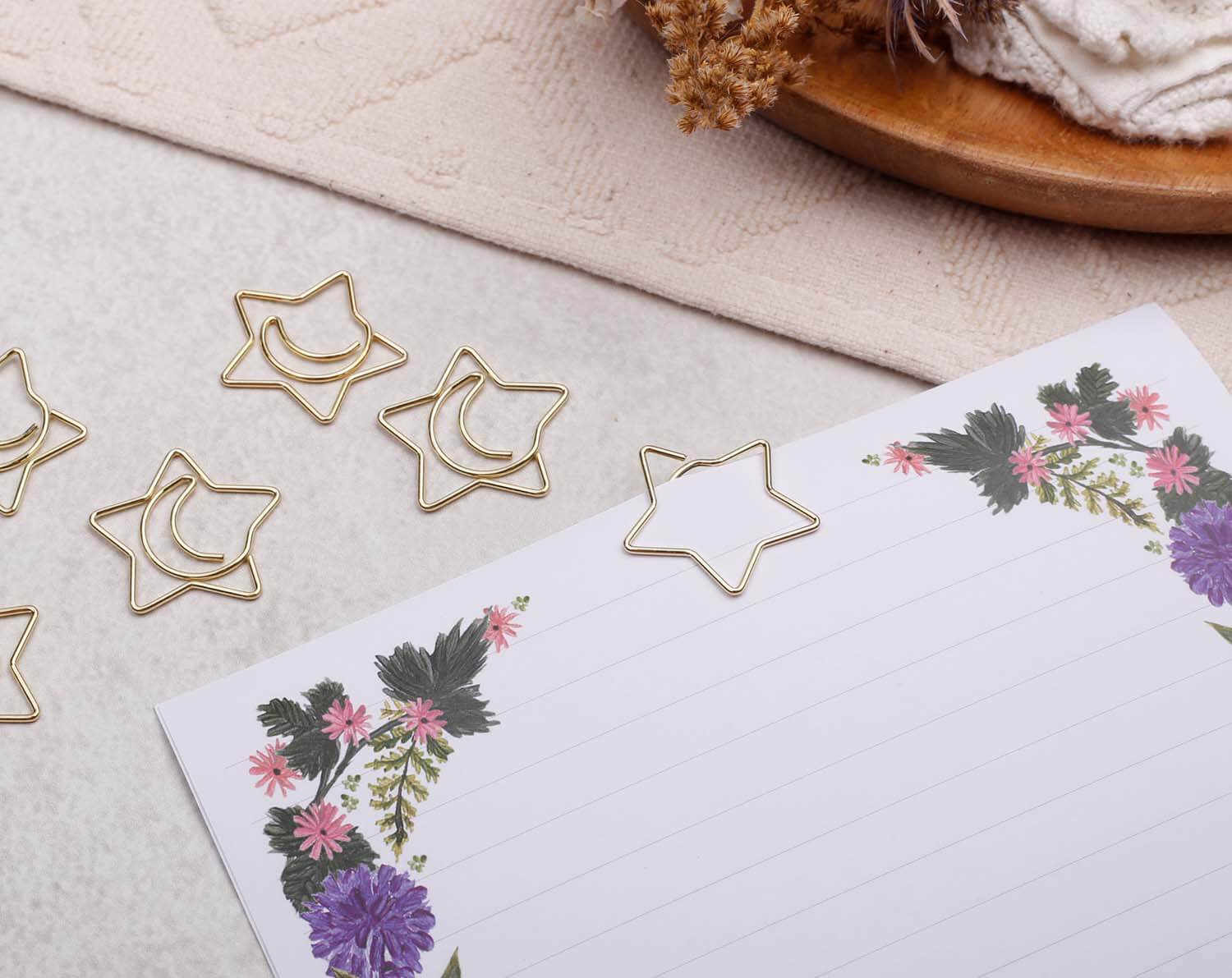 Gold Star Paper Clips arranged on a floral notepad, adding a cheerful touch to stationery.