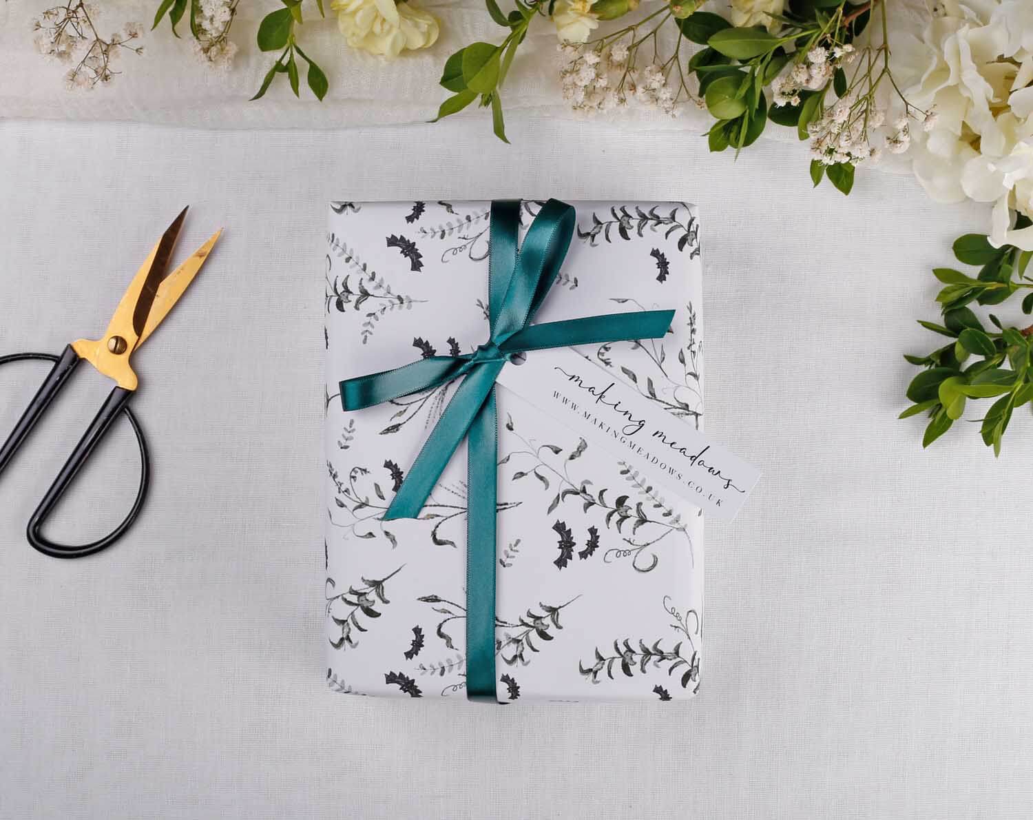 Gothic Wedding Wrapping Paper elegantly wrapped with teal ribbon and tag on a soft white surface surrounded by flowers.