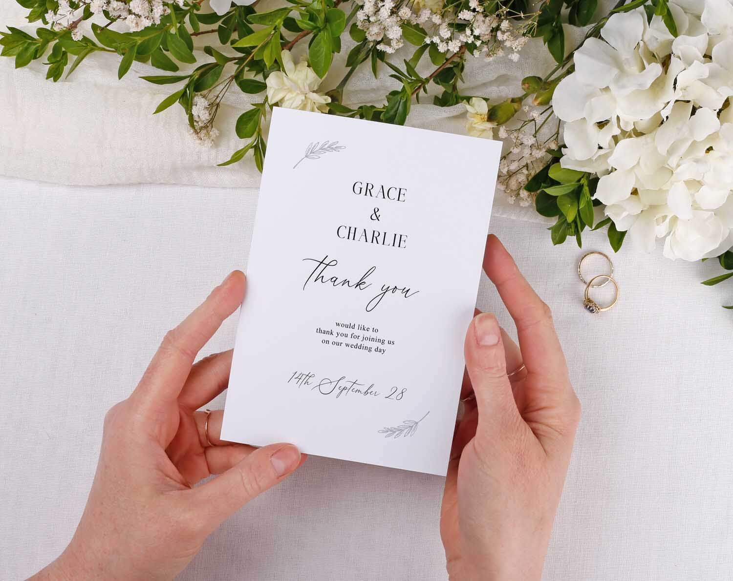 Minimalist Wedding Thank You Cards displayed in hands surrounded by flowers and wedding rings.