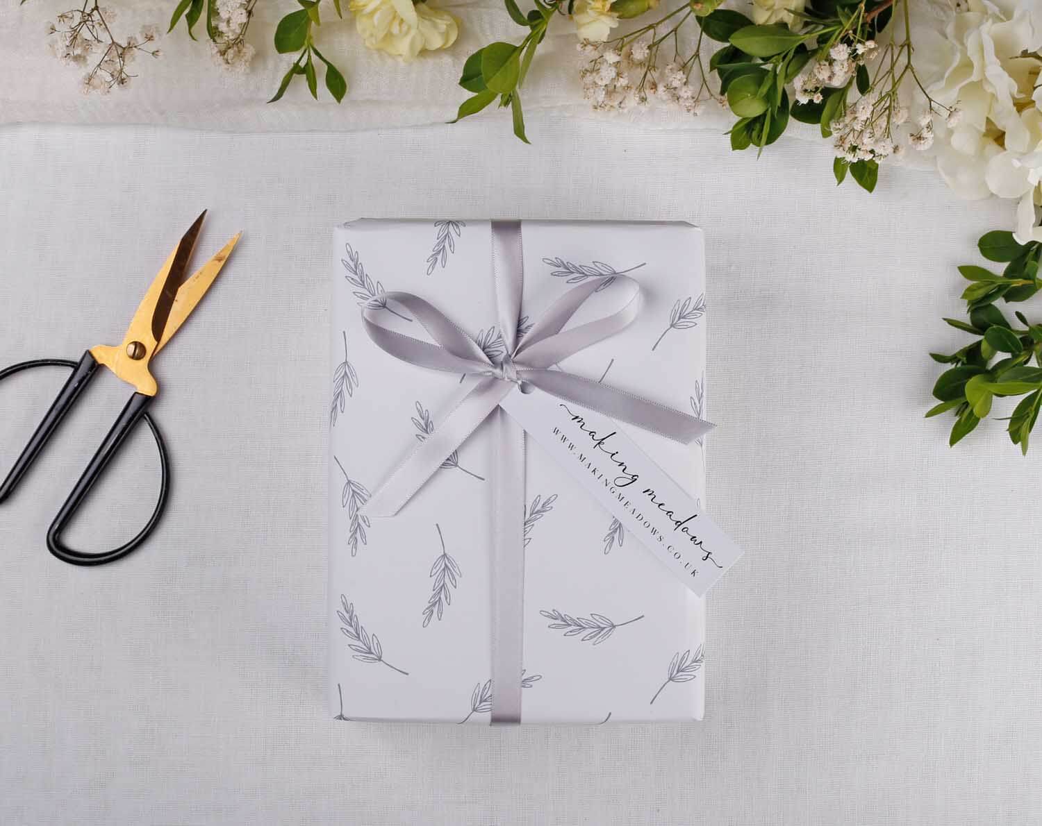 Minimalist Wedding Wrapping Paper gift wrapped with a ribbon and tag, surrounded by floral decorations and scissors.