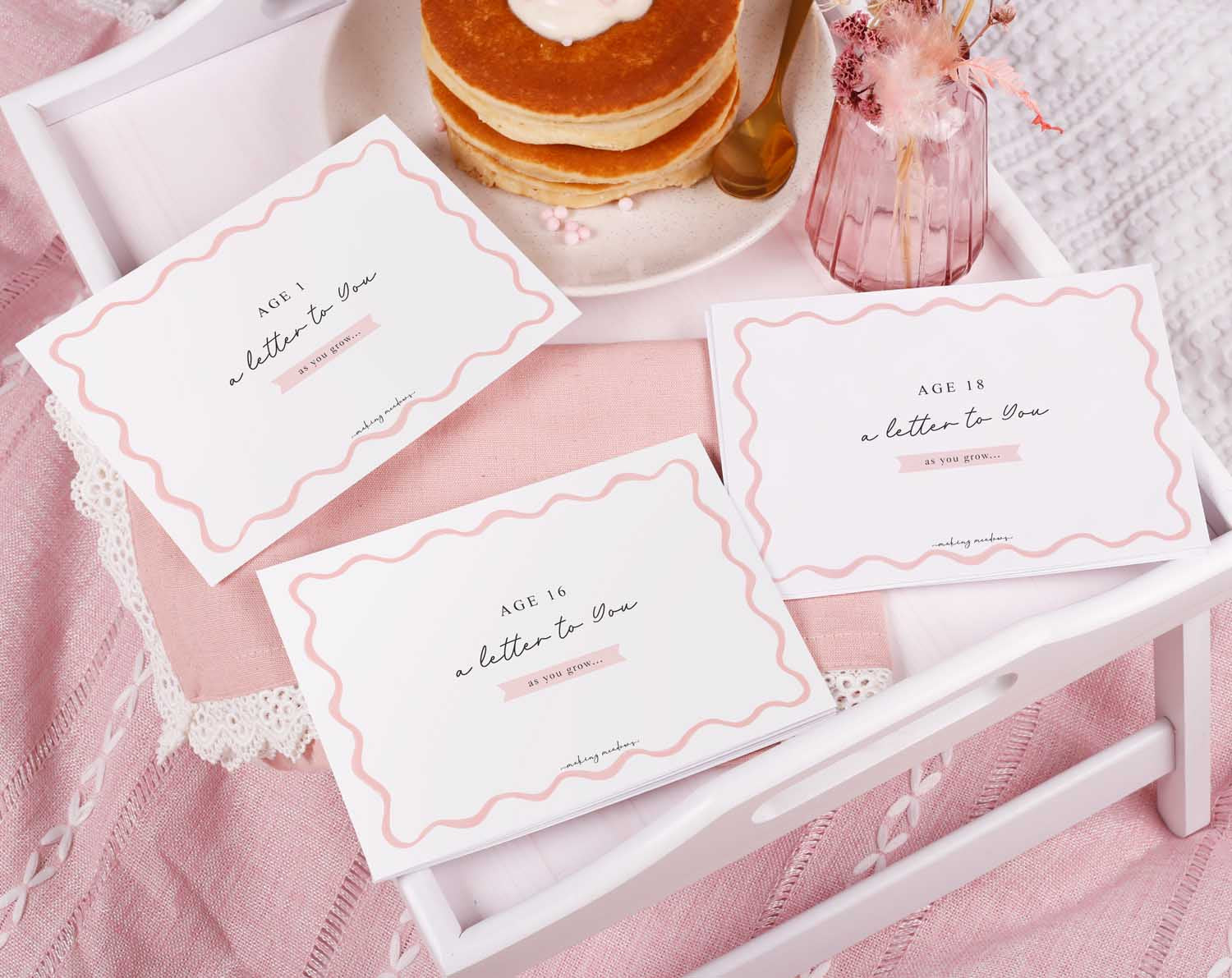 Personalised Pink Wavy Letter To Our Daughter set displayed on a tray with pancakes and flowers.