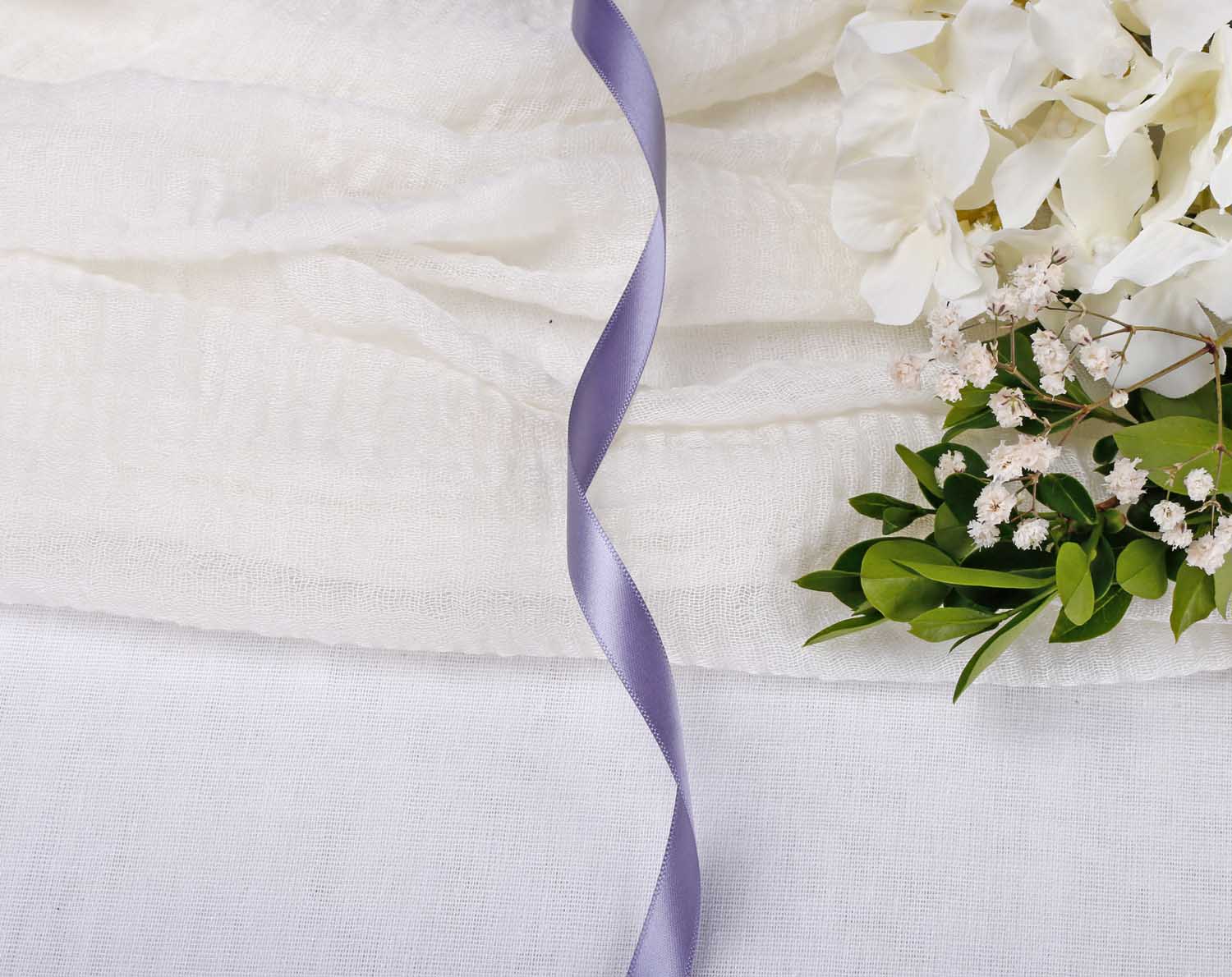 Pewter Satin Ribbon For Wedding draped on soft fabric with white flowers and greenery.