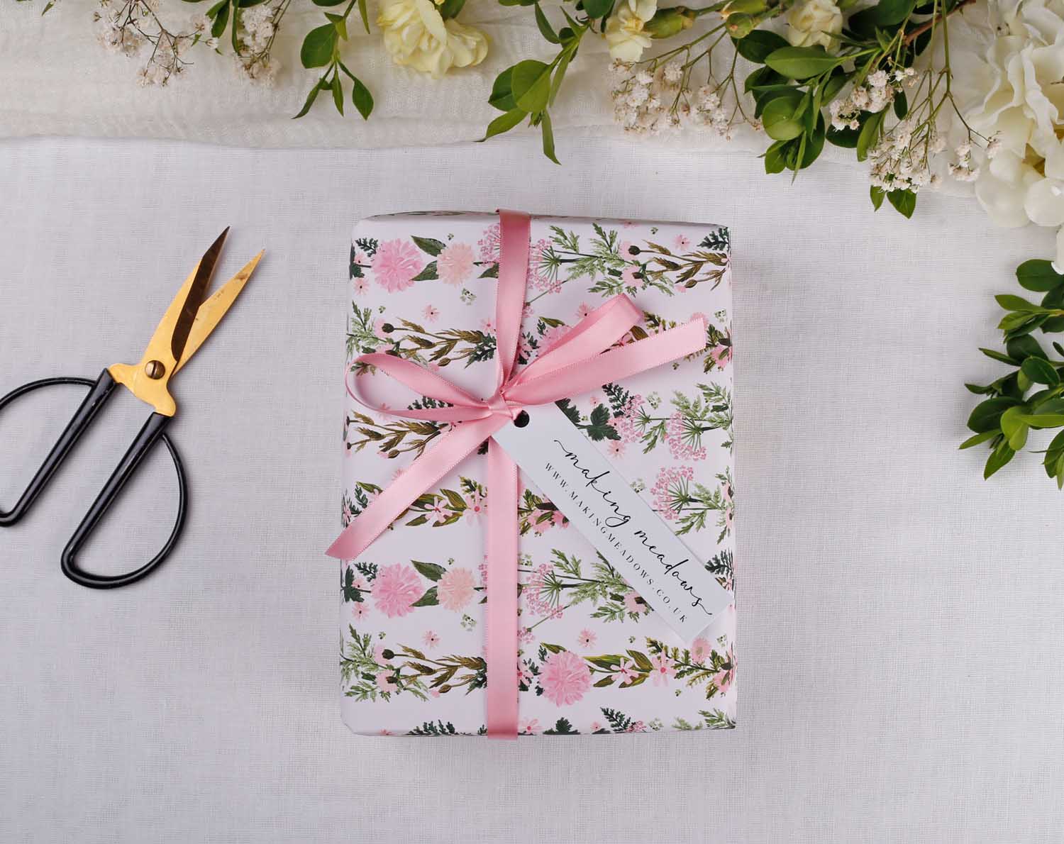 Pink Floral Wedding Wrapping Paper beautifully wrapped with pink ribbon and a gift tag, surrounded by greenery and scissors.
