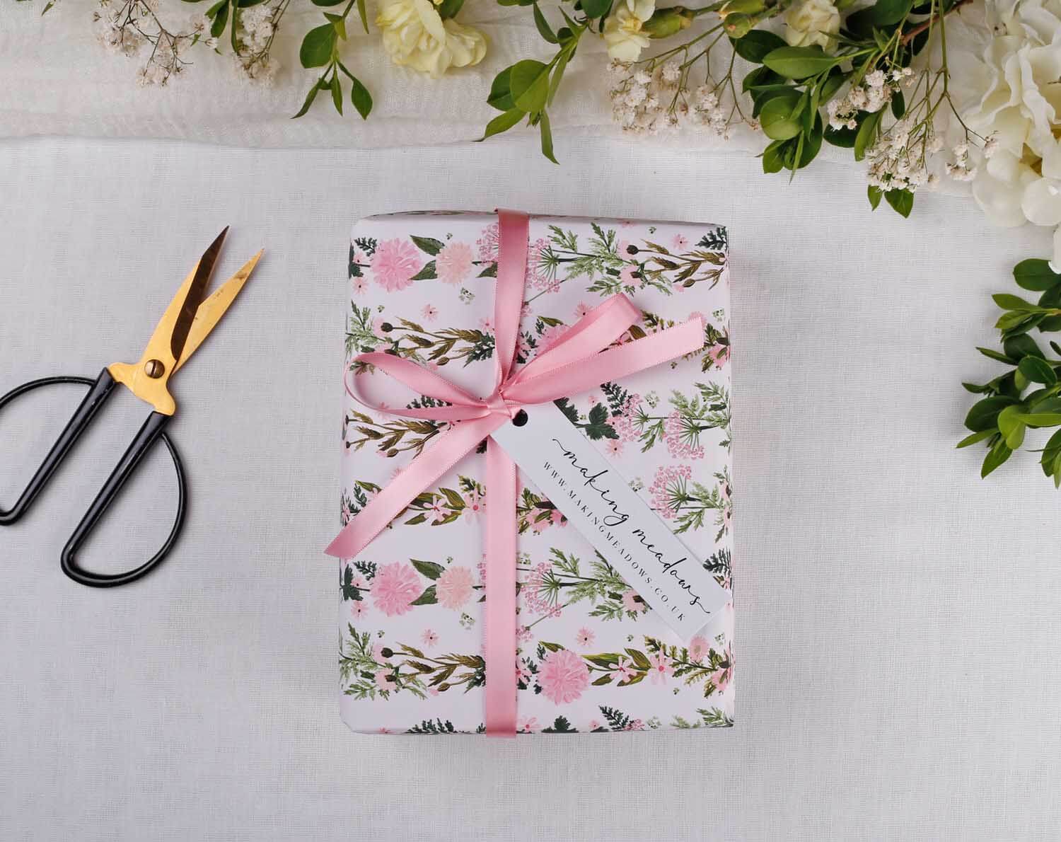 Pink Floral Wedding Wrapping Paper beautifully wrapped with pink ribbon and a gift tag, surrounded by greenery and scissors.