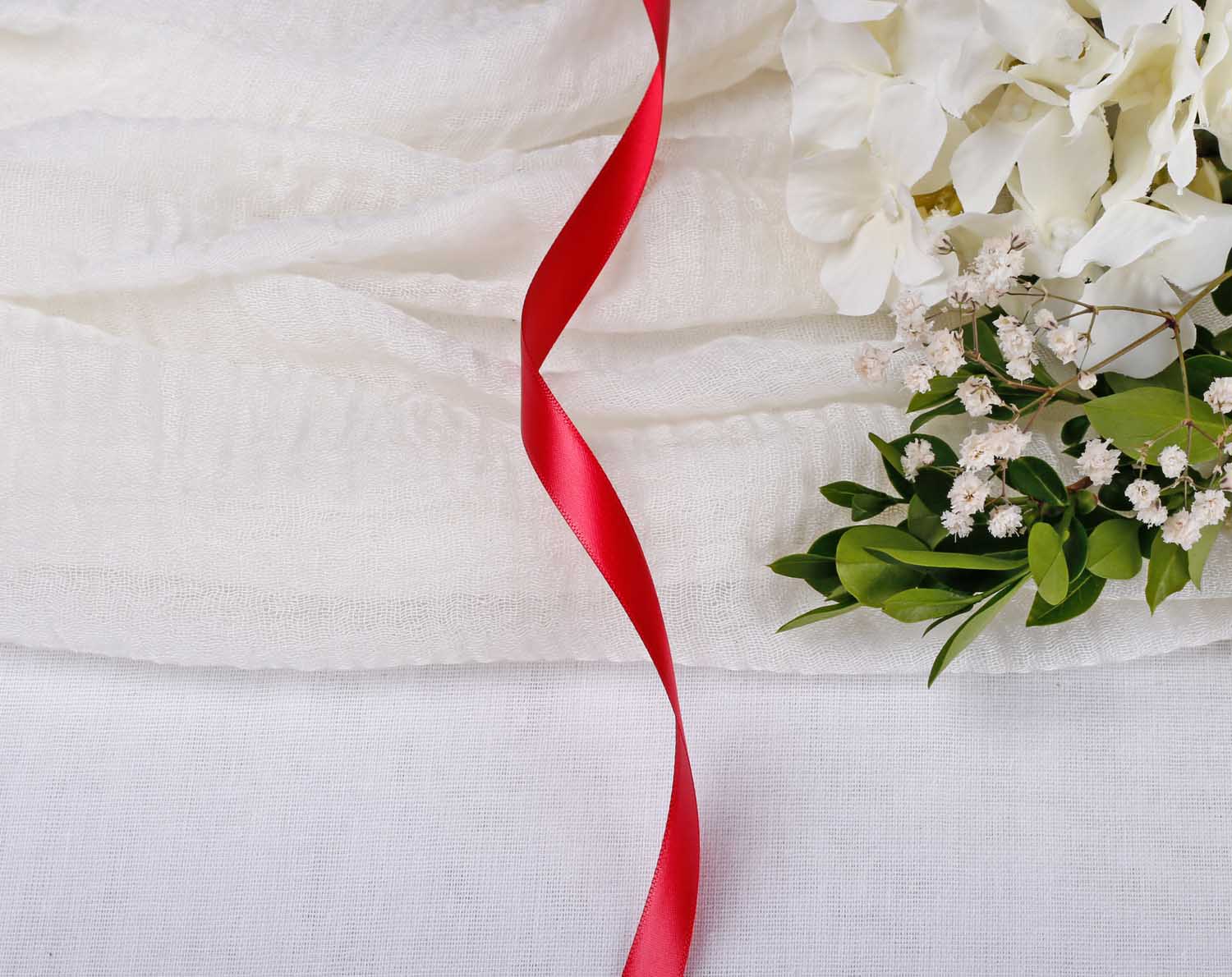 Red Satin Ribbon For Wedding displayed on a white fabric background with flowers.