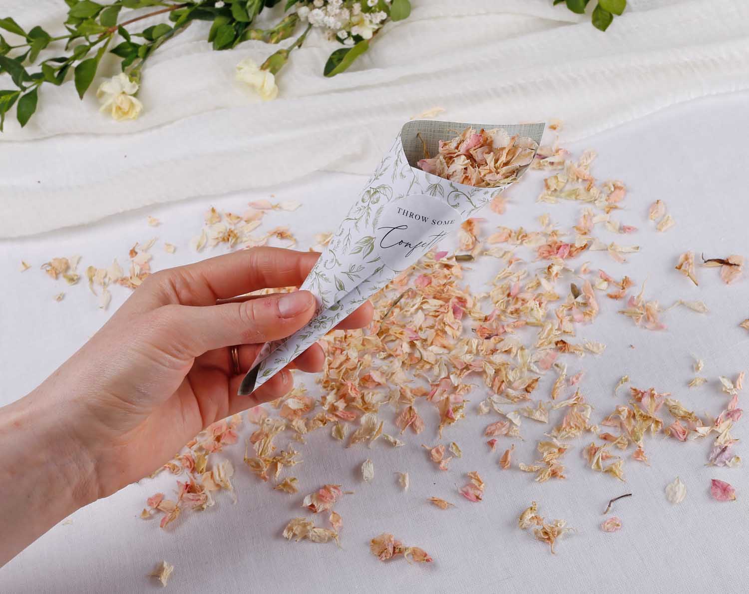 Sage Garden Wedding Confetti Cones filled with flower petals held in a hand with scattered petals on the surface.