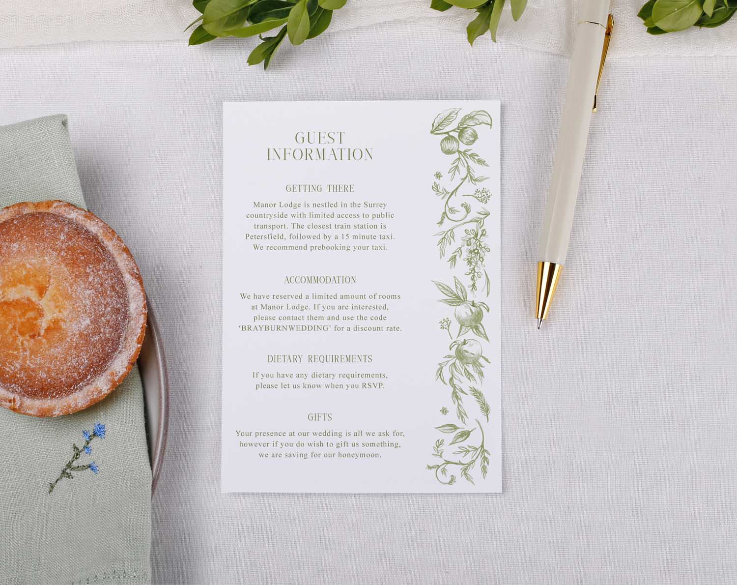 Sage Garden Wedding Information Cards with guest details, featuring greenery design on a table with a pastry and pen.