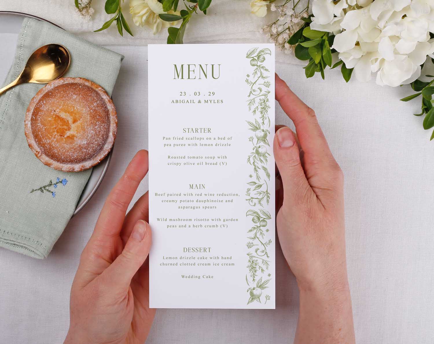 Sage Garden Wedding Menus displayed at a wedding table with floral decorations and a dessert.