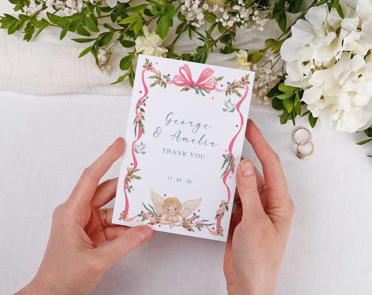 Person holding a Vintage Wedding Thank You Cards with floral design and wedding rings in the background.