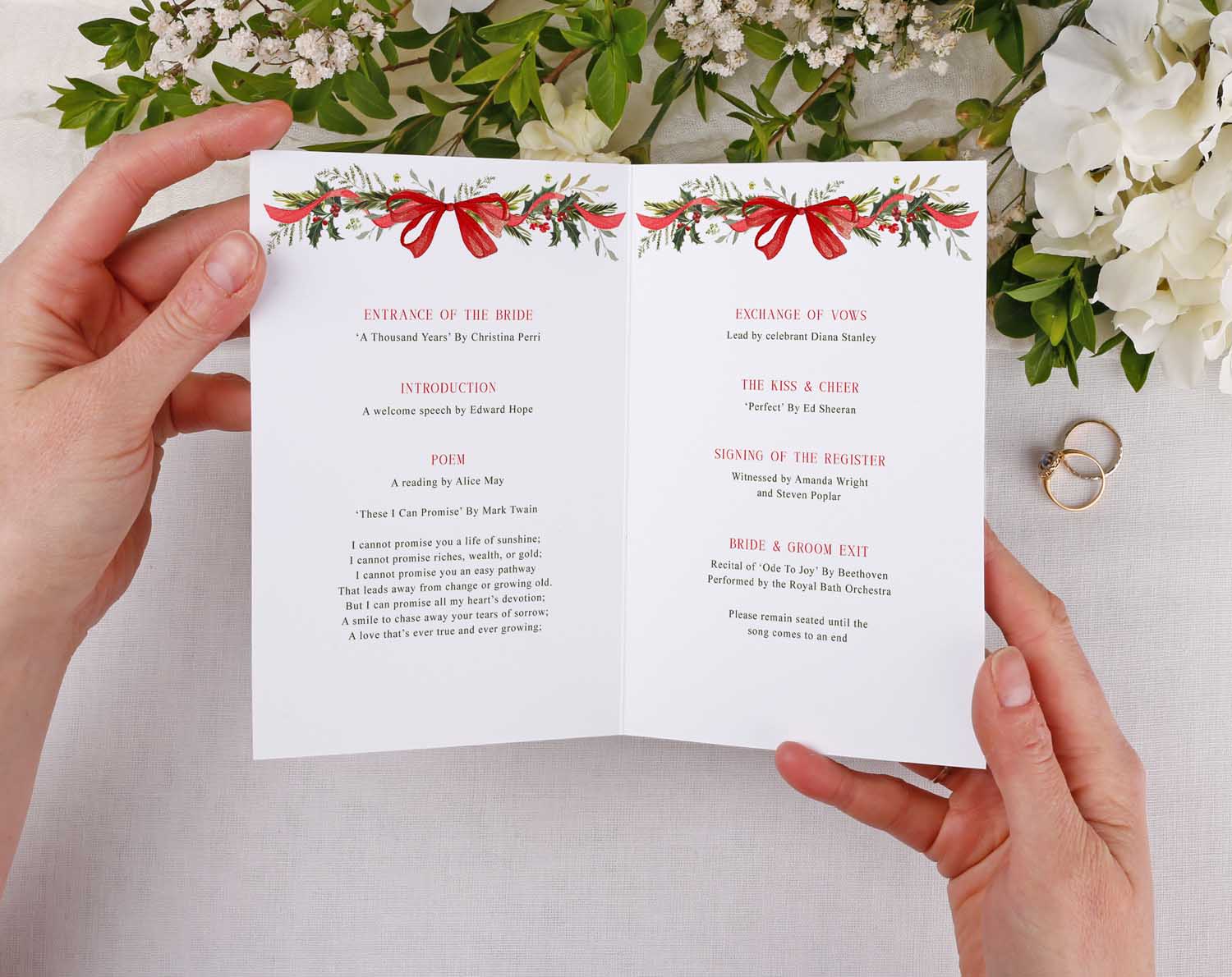 Winter Order Of Service booklet held in hands, featuring winter wedding design with greenery and red bow.