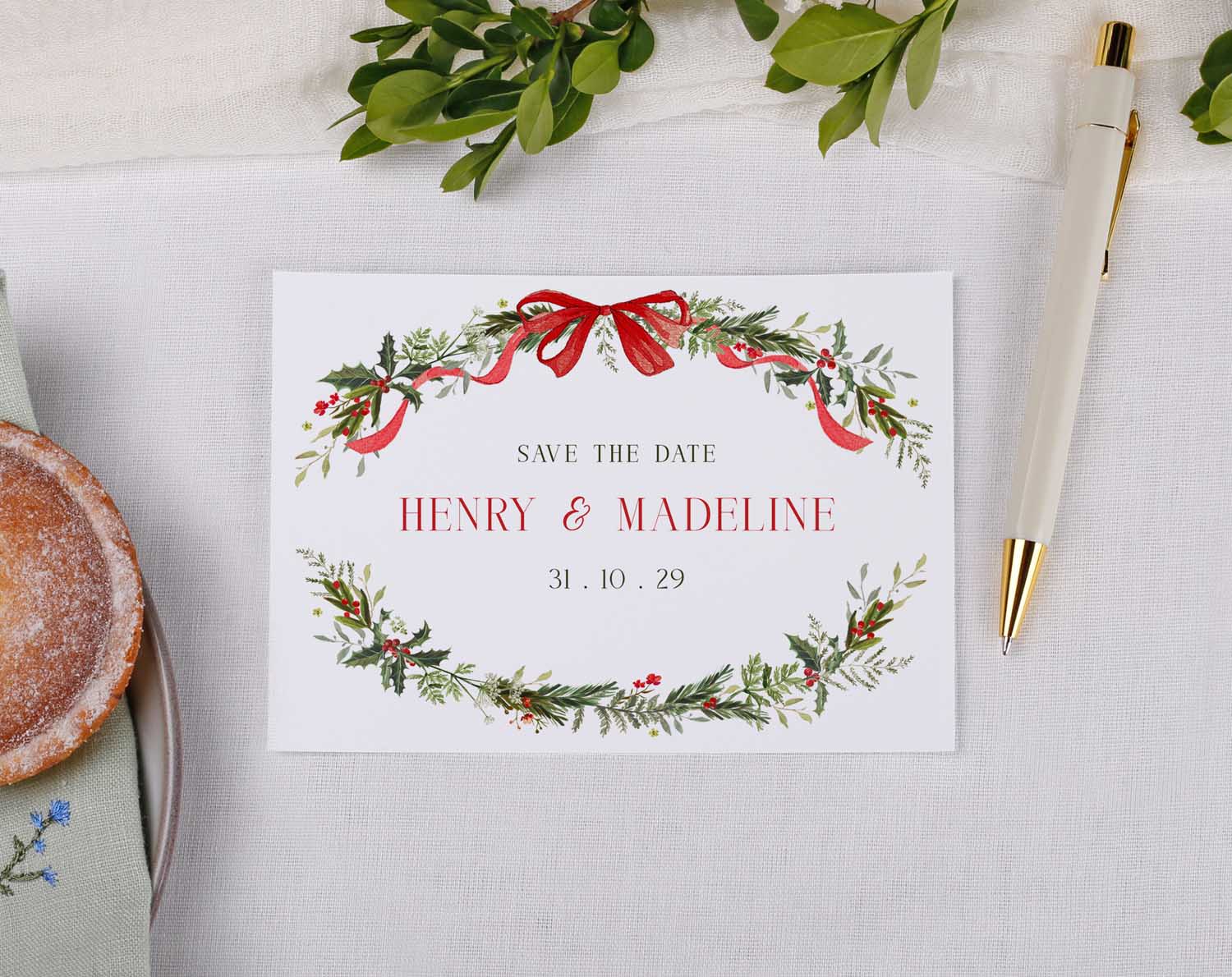 Winter Wedding Save The Date card featuring festive greenery and red ribbons with names and date.