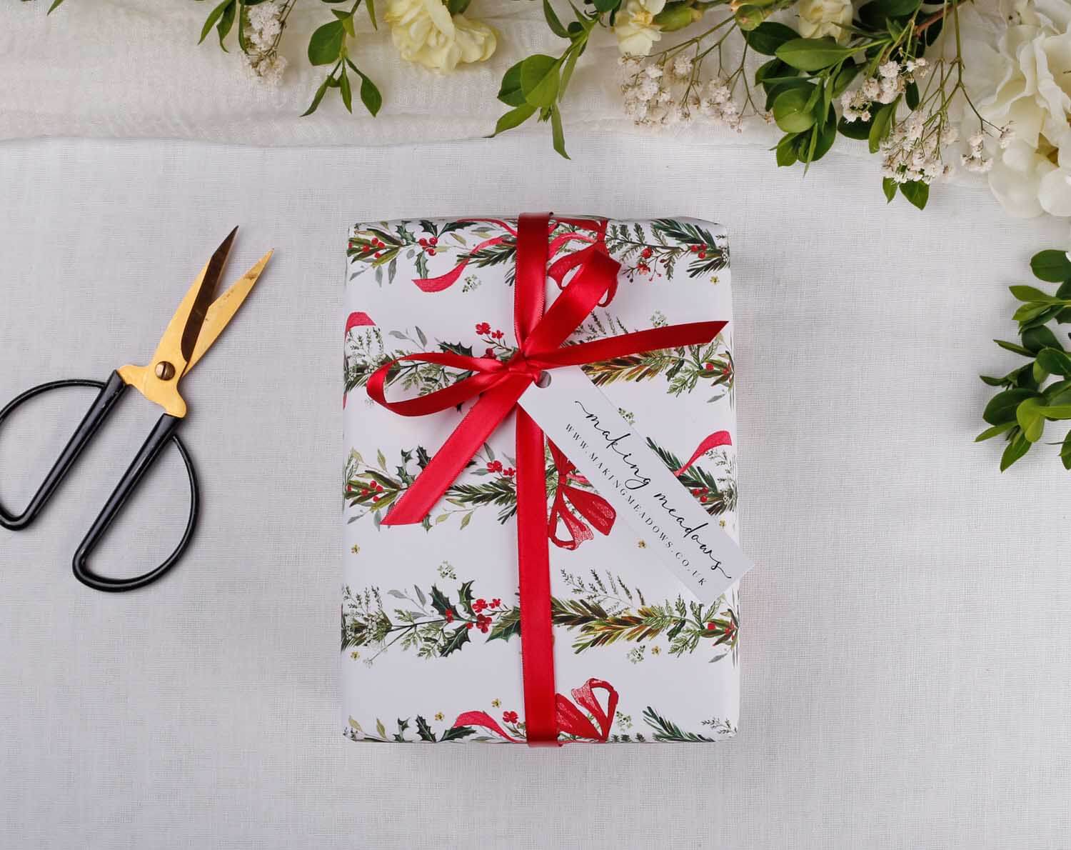 Wrapped gift using Winter Wedding Wrapping Paper adorned with a red ribbon and tag, surrounded by floral accents.