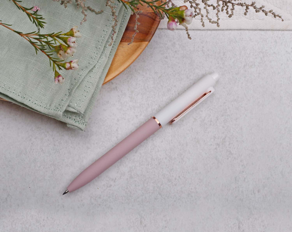 Pink Gel Pen with rose gold trim placed on a light background next to a green napkin and flowers.