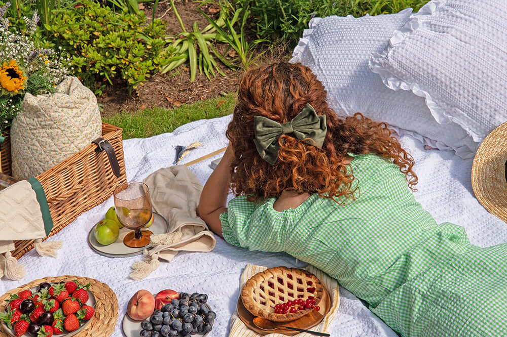The Power of Letter Writing With A Woman relaxing on a picnic blanket with fruits and pie, enjoying nature during a sunny day.
