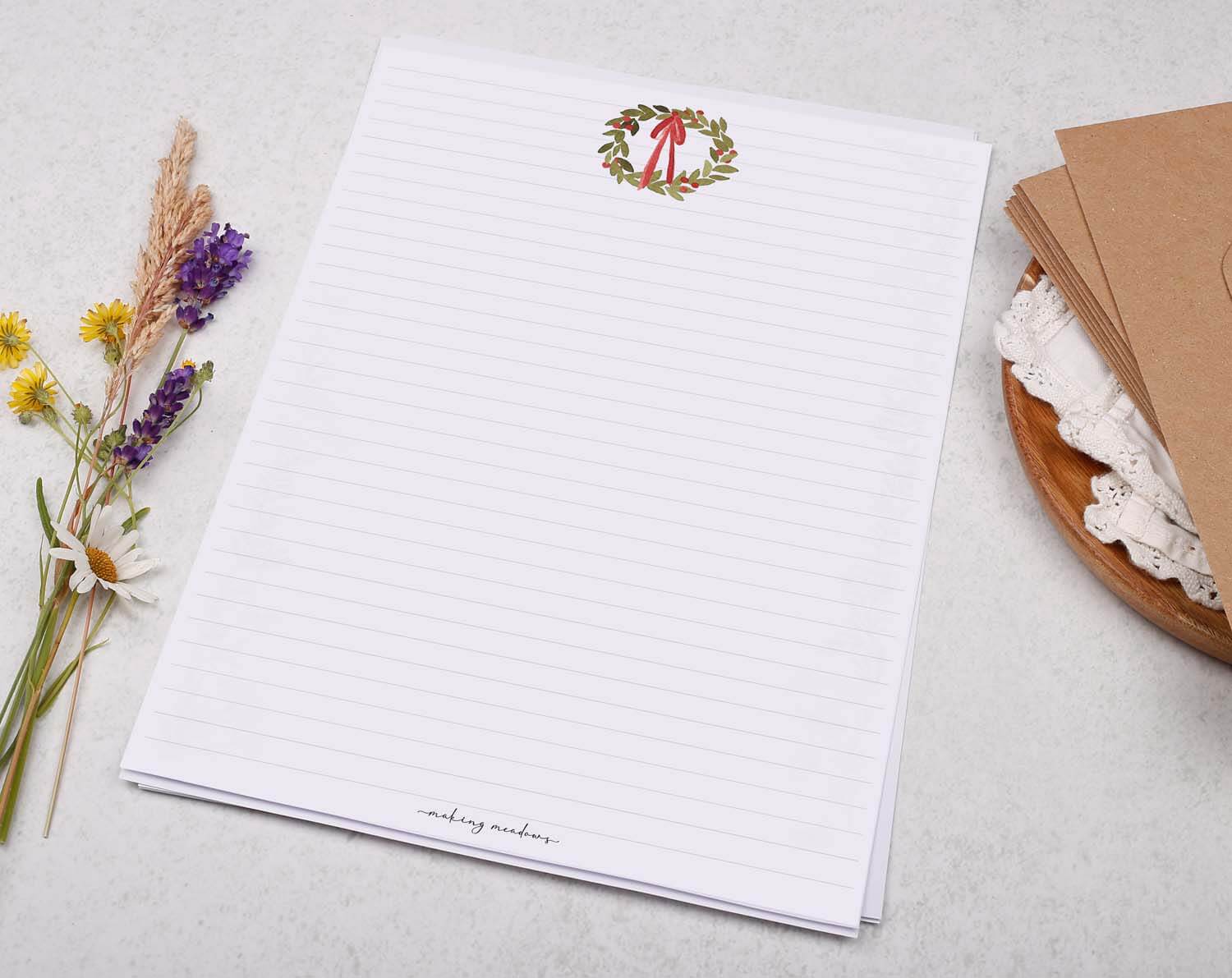 A4 writing paper with Festive Wreath on a table with dried flowers and envelopes, ideal for holiday letters.