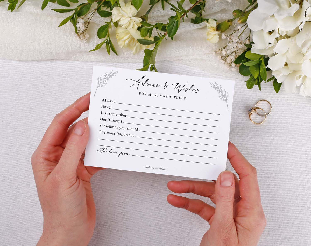 Minimalist Wedding Advice Cards held in hands with floral decor and wedding rings, inviting guest messages.