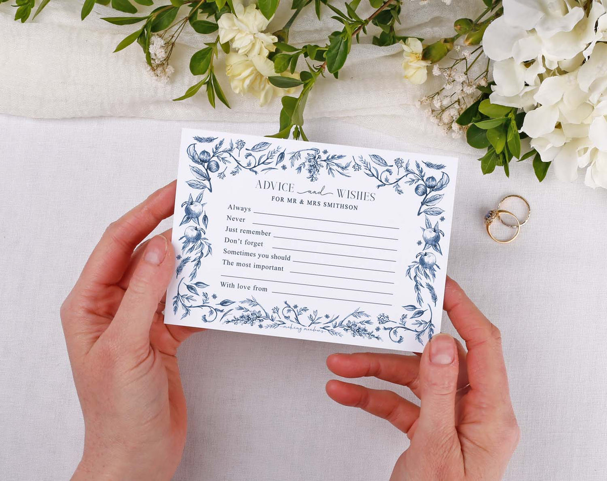 Person holding Blue Garden Wedding Advice Cards with floral design on a table surrounded by wedding decor.