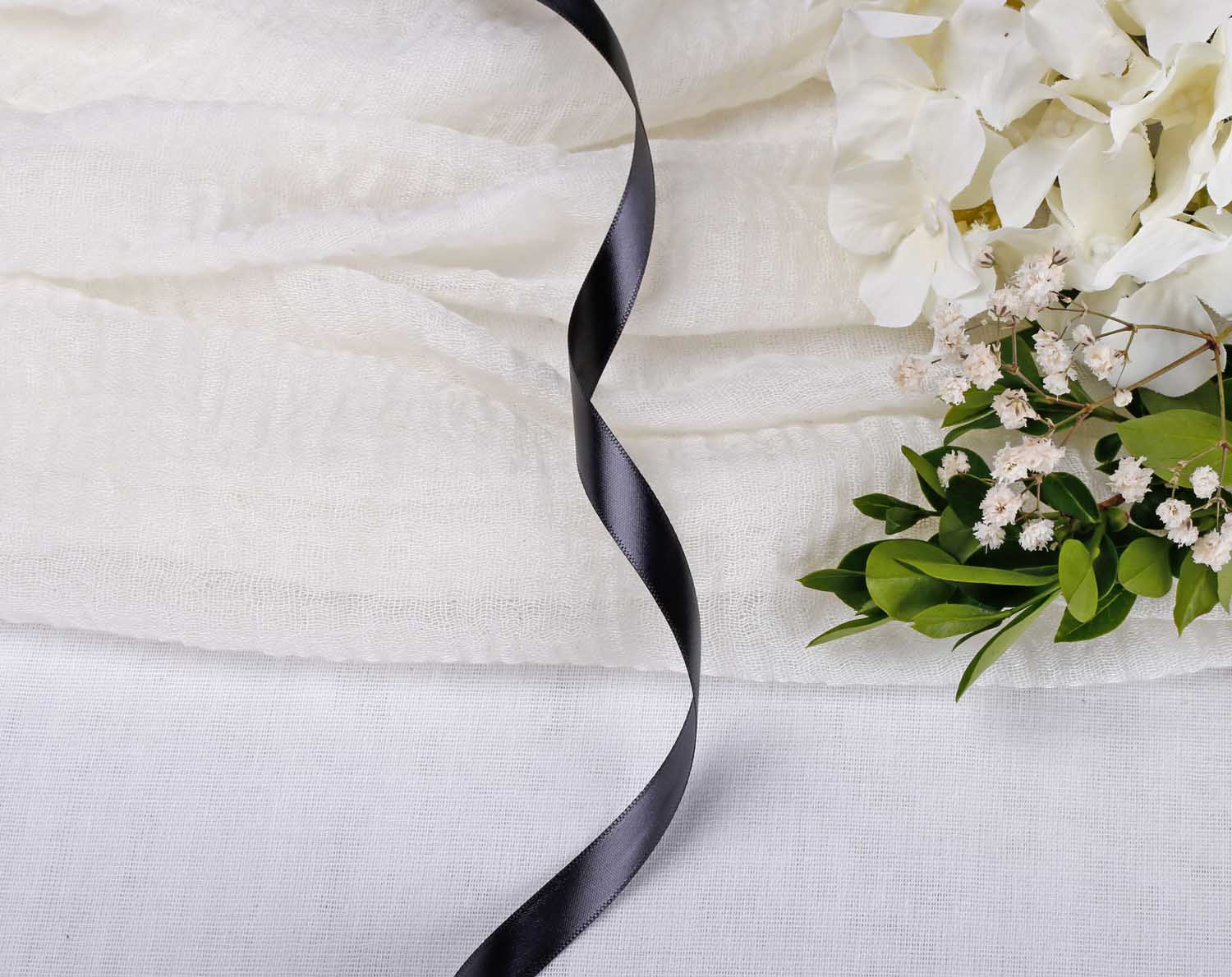 Black Satin Ribbon For Wedding laid elegantly on white fabric with flowers.